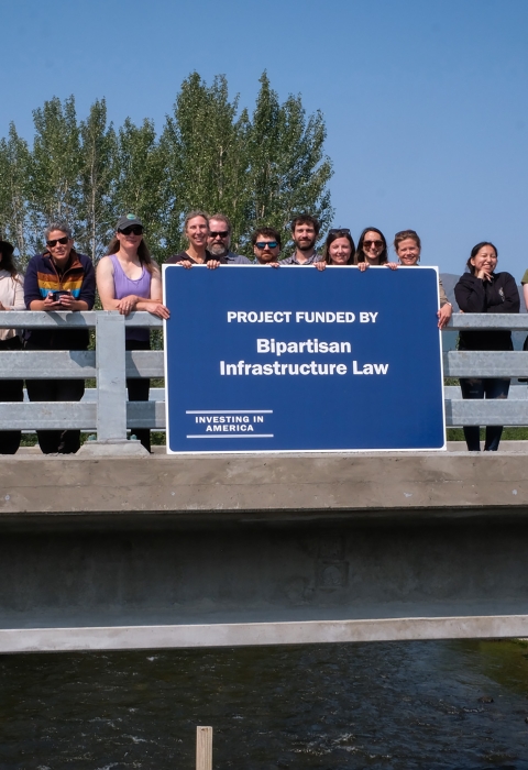 a group of people standing on a bridge over water holding a blue sign