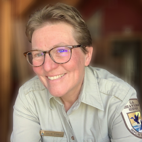 A smiling short-haired woman with glasses, wearing a Service uniform, leans into the photo.