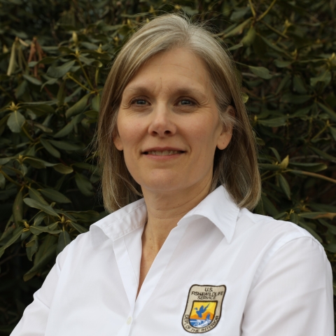 Headshot of Kyla Hastie - a blonde Caucasian woman - outside wearing a shirt with a Fish and Wildlife Service emblem