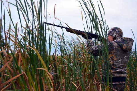 Woman dressed camouflage aims a shotgun into the air