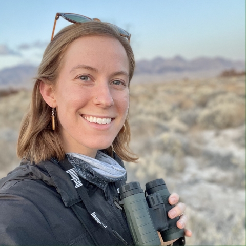 Photo of a woman standing in the desert while holding binoculars