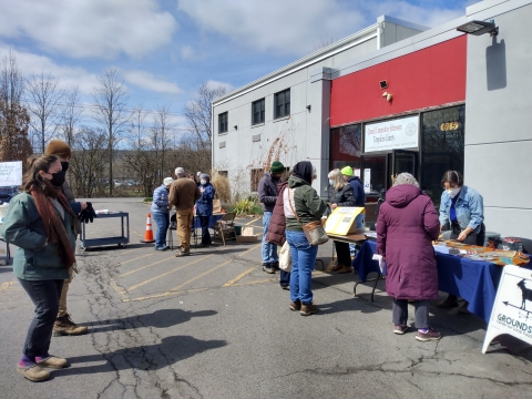 Community members gathered around seed tables outside a building.