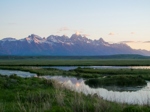 Sunrise over a still pond with distant pointy mountains