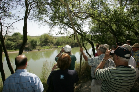 Eight or nine people look at wildlife through binoculars along the river at Santa Ana Refuge.