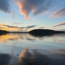 Streaks of brightly lit clouds at sunrise reflect on a body of water with distant islands