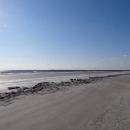 Sunshine reflecting off the water along the grey sandy beach.